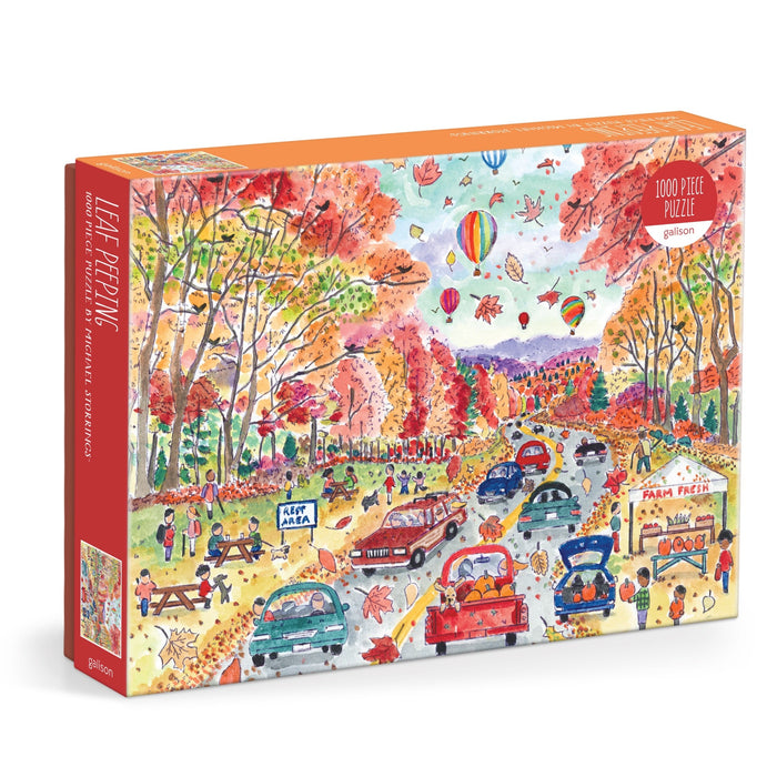 The Michael Storrings Leaf Peeping 1000 Piece Puzzle features a vibrant autumn scene with people driving, walking, and celebrating a fall festival amid colorful trees, hot air balloons, and a farm stand.
