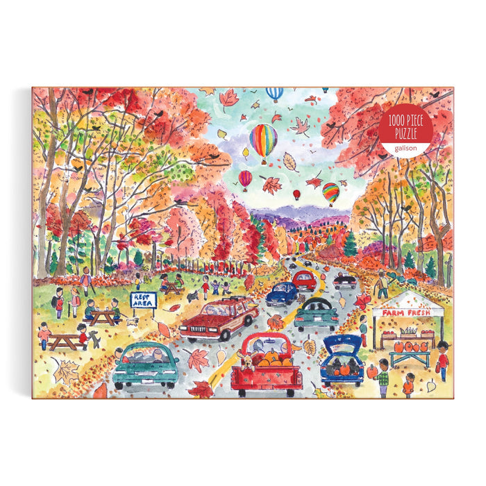 The Michael Storrings Leaf Peeping 1000 Piece Puzzle by Michael Storrings features a vibrant autumn scene with people, cars on a tree-lined road, hot air balloons, and stands selling farm-fresh produce and apple treats.