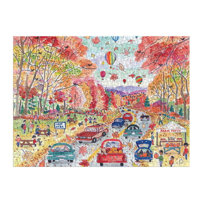The Michael Storrings Leaf Peeping 1000 Piece Puzzle by Michael Storrings showcases cars, people enjoying outdoor fun, picnic tables, a food stand, and hot air balloons floating over scenic autumn foliage.