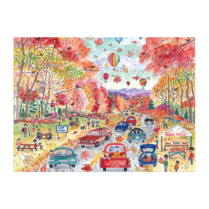 The Michael Storrings Leaf Peeping 1000 Piece Puzzle by Michael Storrings features cars on a fall road, picnickers, farm stand shoppers, hot air balloons drifting above, and vibrant autumn leaves blanketing the ground.