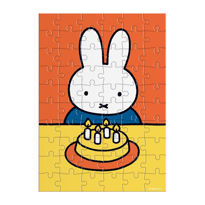 The Miffy Birthday Greeting Card Puzzle by Miffy features a white cartoon bunny with upright ears at a table, celebrating with a yellow cake topped with five lit candles against an orange and yellow background.