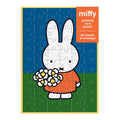 The Miffy with Flowers Greeting Card Puzzle by Miffy features a white cartoon bunny in an orange dress holding flowers on green grass with a blue sky. Includes 60 pieces and an envelope—perfect as a unique greeting card and puzzle gift.