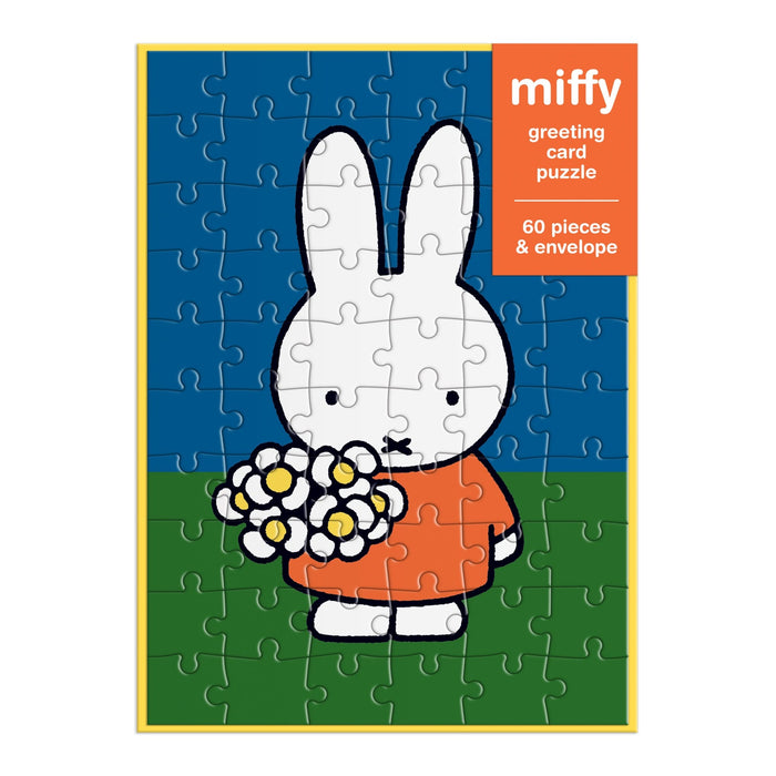 The Miffy with Flowers Greeting Card Puzzle by Miffy features a white cartoon bunny in an orange dress holding flowers on green grass with a blue sky. Includes 60 pieces and an envelope—perfect as a unique greeting card and puzzle gift.