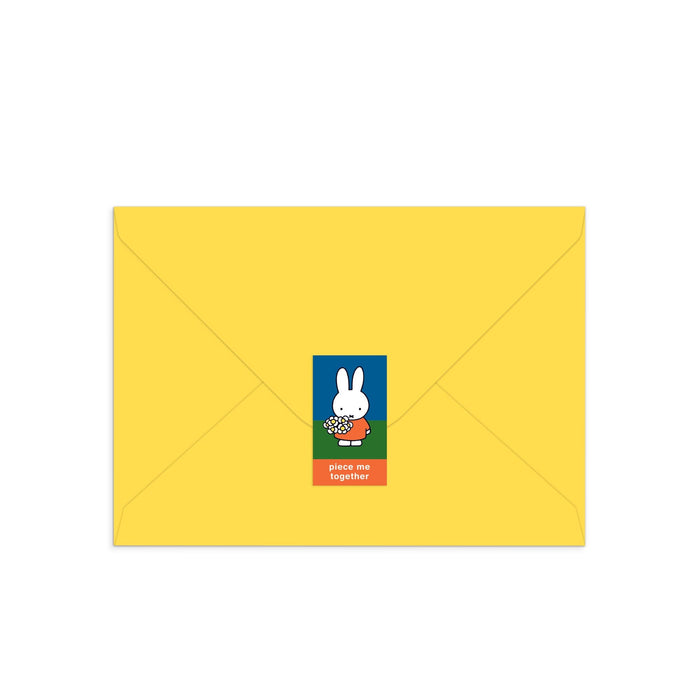 A closed yellow envelope displays a center sticker with Miffy, the white cartoon rabbit, holding flowers and “piece me together” on a red background. Product: Miffy with Flowers Greeting Card Puzzle by Miffy.