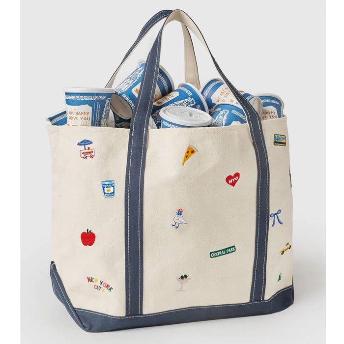 Natural cotton canvas tote bag with various NYC icons embroidered, filled with paper greek cups, front angle view, on a gray background.
