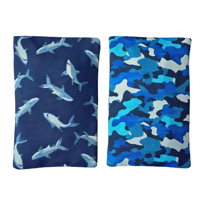 Two soft gel ice packs with fabric sleeves, one with a blue camouflage print and the other with a shark print, shown side by side on a plain white background.