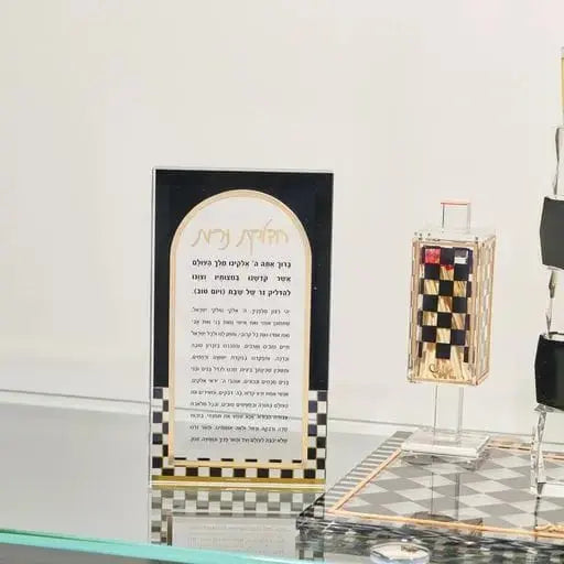 Onyx Hadlokas Neiros card with gold checkered border displayed on shelf, lucite candle-lighting instruction card for Shabbat hostess gifts.