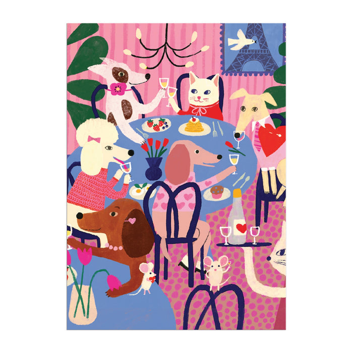 The Paws for Love Greeting Card Puzzle by Anne Bentley features a colorful scene of dogs and a cat around a blue table with food, drinks, flowers, wine glasses, and the Eiffel Tower in the background.