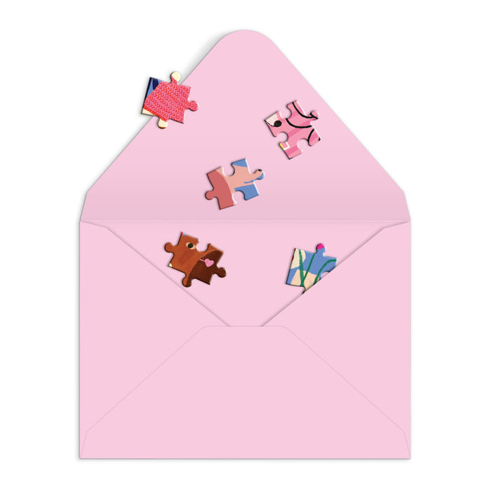 The Anne Bentley Paws for Love Greeting Card Puzzle features a pink envelope, open to reveal five vibrant pet-themed jigsaw pieces scattered in and around the flap, all set against a clean white background.