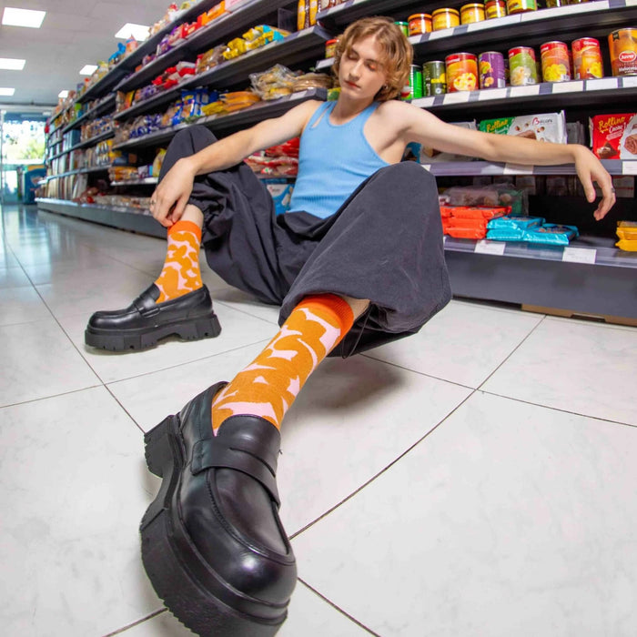 Person sitting on the floor of a grocery store aisle wearing orange socks with pink patterns.