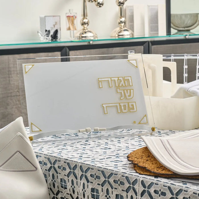 Pearlstone Haggadah Stand in pearl marble with gold text, displayed on a dining table with place settings and Passover tableware for Pesach.