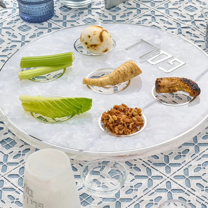 Pearlstone Seder plate with pearl marble finish displaying traditional Passover foods in compartments, set on decorative blue and white tablecloth for holiday table.