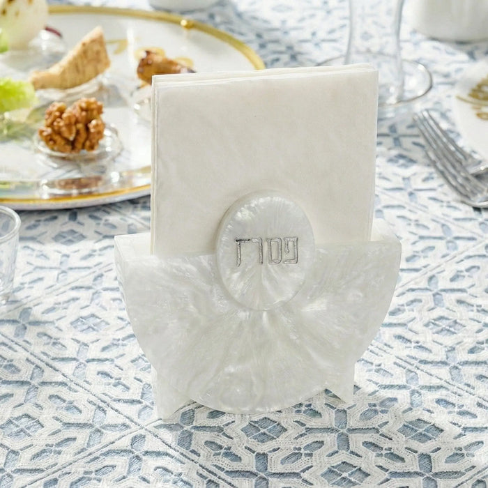 Cream resin Pesach napkin holder with embossed Hebrew text, displayed on a patterned tablecloth with holiday tableware
