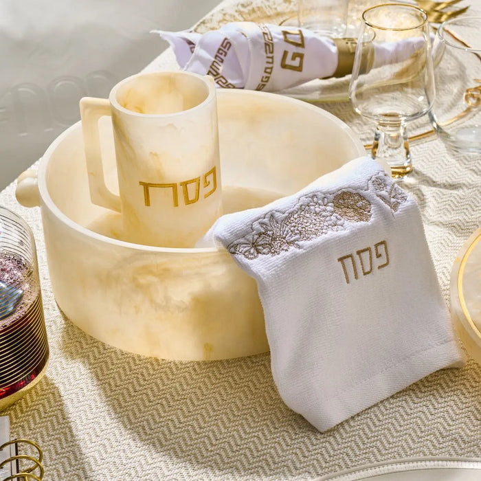 Cream resin Pesach washing cup with gold accents and matching towel on display table for Passover.