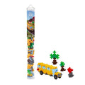 A clear plastic tube of small building blocks stands next to a assembled yellow school bus model with small trees, on a plain white background. The tube label shows the brand name 'Plus Plus'.