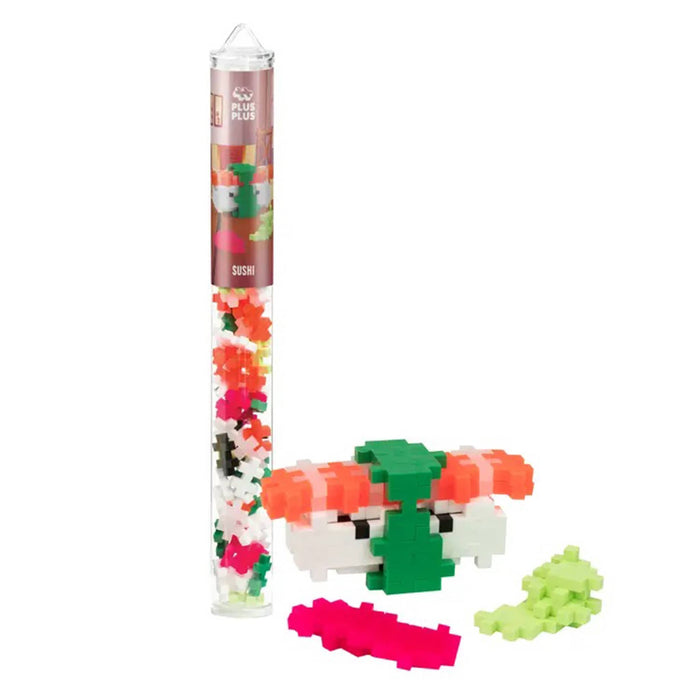 A clear cylindrical tube filled with small multicolored building blocks stands next to an assembled sushi figure on a plain white background. The tube label shows the brand name 'Plus Plus" and the word 'sushi'.