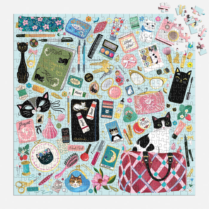 The Purrfect Accessories 500 Piece Foil Puzzle by Christine De Carvalho features cats, books, makeup, flowers, and vintage items on a light blue background, with a few unplaced pieces remaining in the top right.