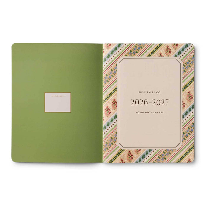 An open 2026-2027 academic planner from Rifle Paper Co., showing a solid sage green left cover with a name label and a right cover featuring a multicolor geometric and floral pattern with a cream center panel.