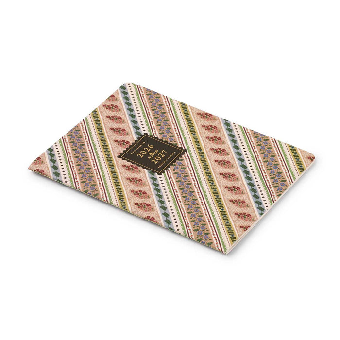 A 2026-2027 academic planner with a rose, green, and blue ribbon-striped patterned cover featuring diagonal bands of floral motifs and a central dark brown label, side and top view on a white background.