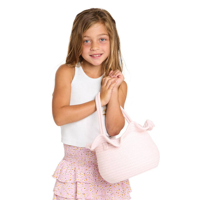 Young girl holding a pink woven basket with ruffle and handle against a white background.
