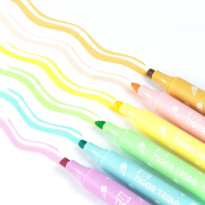 Six dual-tip marker pens in pastel and warm colors, each drawing a thin and thick wavy line of the same color on a white background. The pens are labeled 'TIGER TRIBE'.