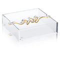 Clear acrylic Shabbos napkin holder with gold-toned wavy metal handle design, perfect for table settings.