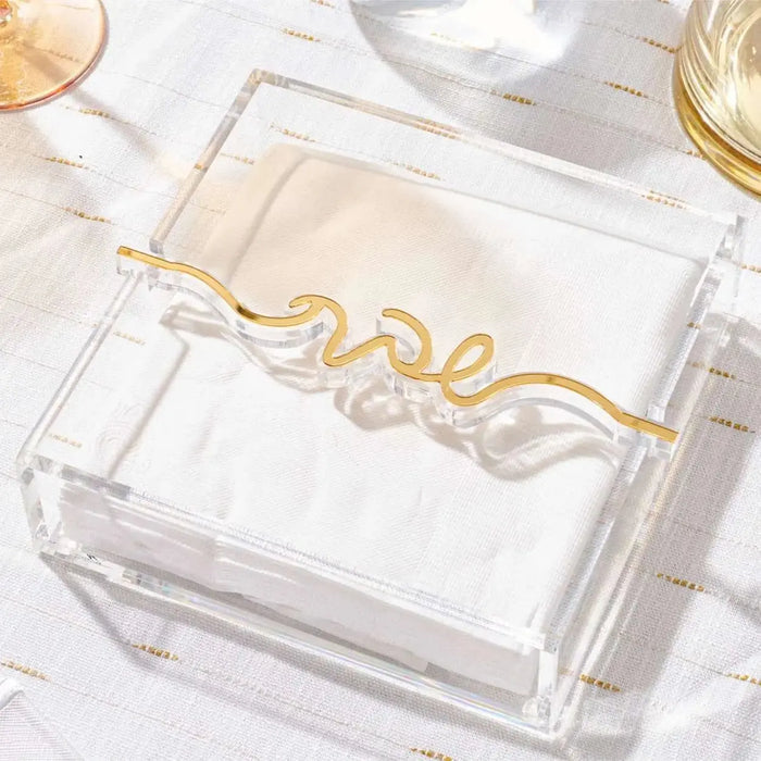 Gold "love" Shabbos Bar napkin holder with white napkins on white tabletop with glasses