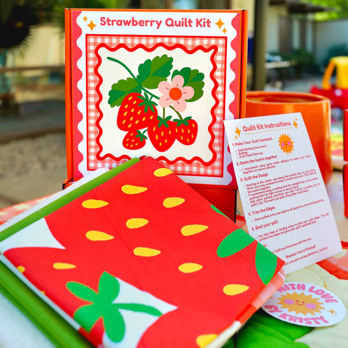 Strawberry quilt kit with contents and instructions on a table outdoors.