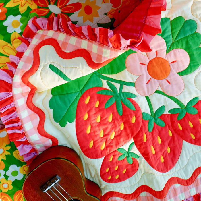 Colorful quilt with strawberry pattern and ukulele on a floral background.