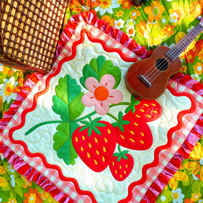 Colorful quilt with strawberry design and ukulele on a floral background.