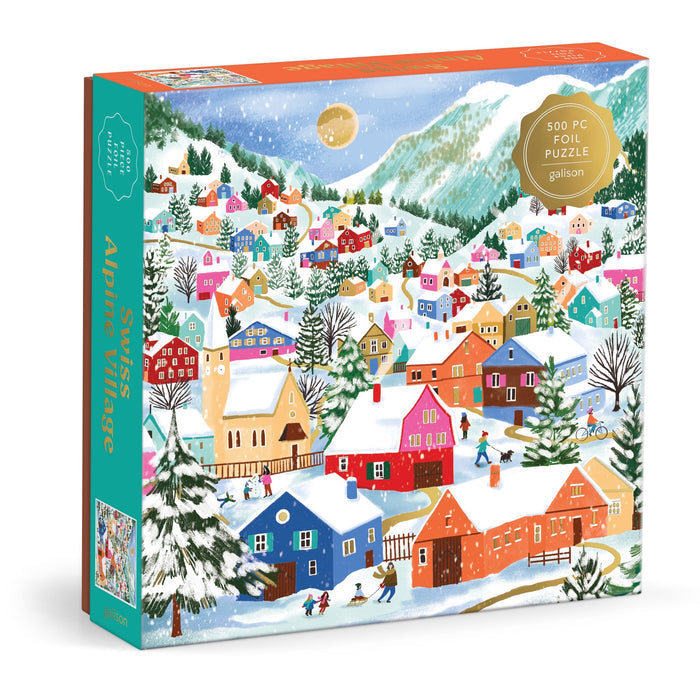 The Joanna Clay Swiss Alpine Village 500 Piece Foil Puzzle features a vibrant snowy village scene with painted houses, sledding people, snow-capped mountains, and a golden moon in the background.