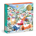 The Joanna Clay Swiss Alpine Village 500 Piece Foil Puzzle features a vibrant snowy village scene with painted houses, sledding people, snow-capped mountains, and a golden moon in the background.