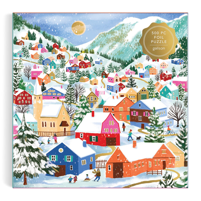 A vibrant winter village scene with colorful houses, snowy rooftops, skaters, skiers, pine trees, and mountains. A gold sticker marks this as the Swiss Alpine Village 500 Piece Foil Puzzle by Joanna Clay.