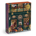 The Gilded Spine 1000 Piece Foil Puzzle by Sally Wilson depicts a charming bookstore with large windows, shelves of books, autumn leaves, cozy lights, a black cat, and a dog inside and outside the shop.