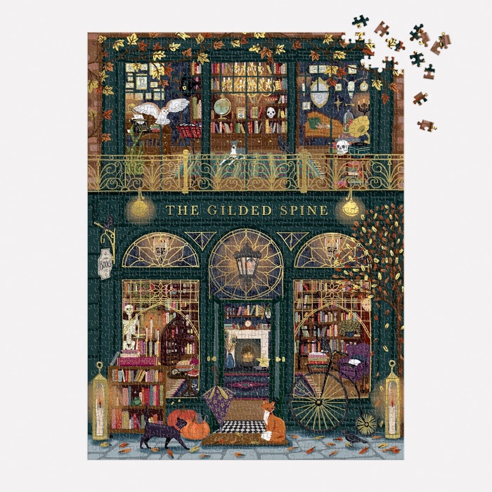 The Gilded Spine 1000 Piece Foil Puzzle by Sally Wilson features a cozy bookstore with cats, books, glowing lamps, and missing pieces in the top right corner. A dog and fox sit at the entrance, adding to the charming scene.