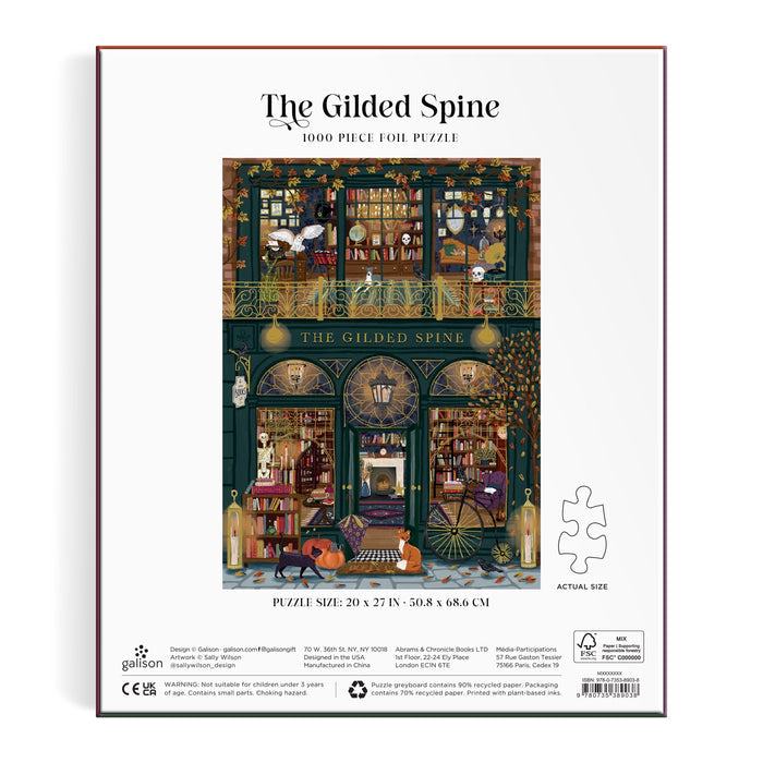 The Gilded Spine 1000 Piece Foil Puzzle by Sally Wilson features a cozy bookstore scene with bookshelves, hanging lights, readers, and a cat by the door. Finished puzzle measures 20 x 27 inches.