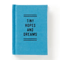 The Brass Monkey Tiny Hopes and Dreams Tiny Diary is a small, blue hardbound notebook with Tiny Hopes and Dreams in black on the cover, along with decorative lines. Photographed against a white background.