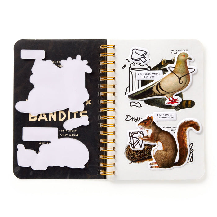 An open spiral notebook displays Brass Monkey’s Trash Bandits Sticker Book stickers—featuring pigeons and squirrels holding envelopes and speech bubbles with funny mail messages—on the left page.