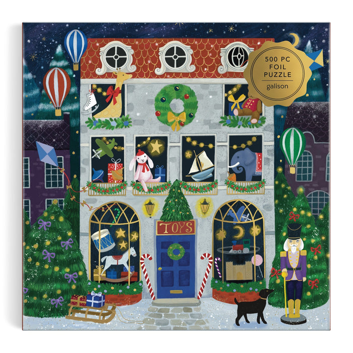 The Bex Parkin Twilight Toy Shop 500 Piece Foil Puzzle features a festive toy shop with wreaths, lights, candy canes, toys in the windows, hot air balloons above, a nutcracker and black cat outside—all beneath falling snow.