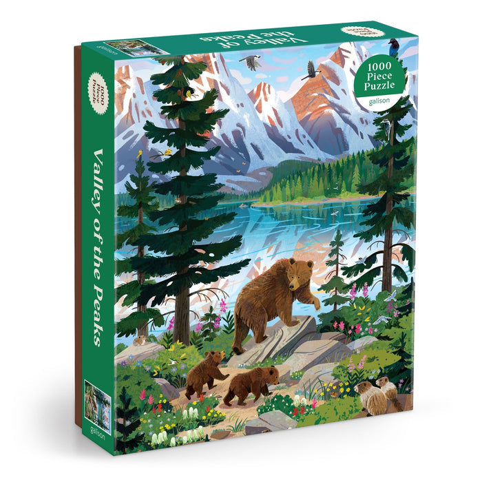 The Kim Smith Valley of the Peaks 1000 Piece Puzzle features a bear with cubs walking by a mountain lake, with snow-capped peaks and wildlife in the background.