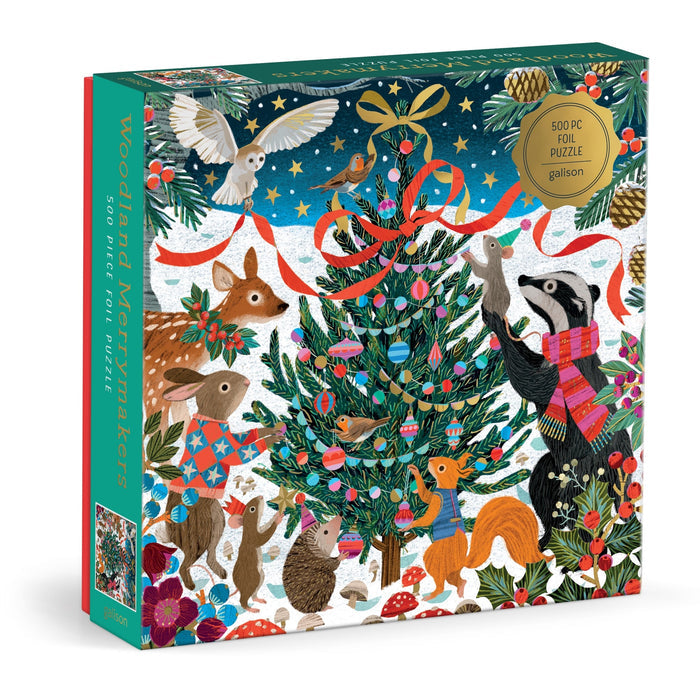 The Victoria Ball Woodland Merrymakers 500 Piece Foil Puzzle by Victoria Ball features woodland animals like a badger, fox, deer, and owl decorating a Christmas tree in a snowy, festive scene with bright colors and pine branches.