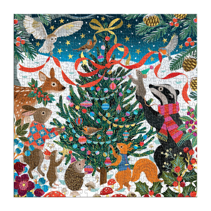 The Victoria Ball Woodland Merrymakers 500 Piece Foil Puzzle by Victoria Ball features woodland animals like a deer, rabbit, hedgehog, fox, and badger around a festive Christmas tree in the snowy outdoors with ornaments, ribbons, and birds.