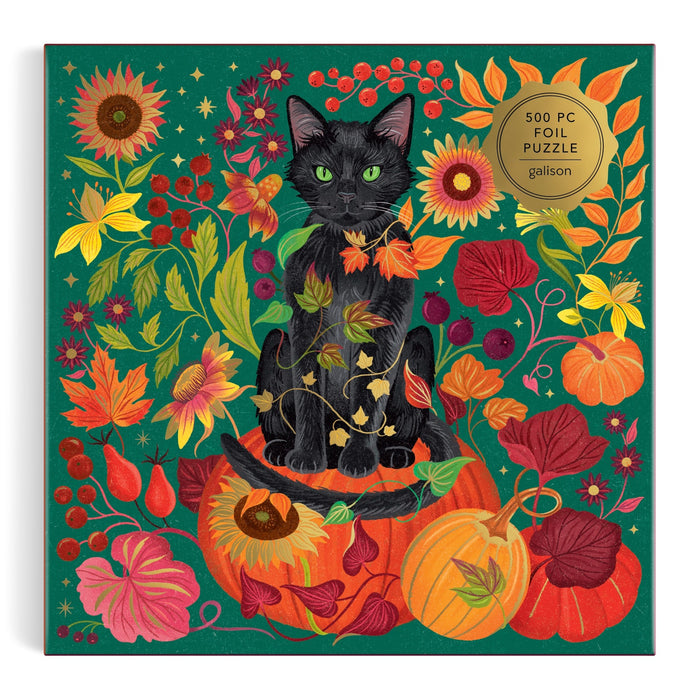 The Dawn Cooper "Whiskers of Autumn" 500 Piece Foil Puzzle features a black cat on a pumpkin amid vibrant autumn leaves, flowers, berries, and vines set against a green background.