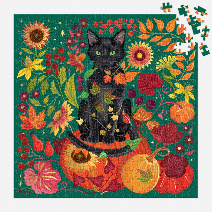 The Whiskers of Autumn 500 Piece Foil Puzzle by Dawn Cooper features a black cat on pumpkins amid autumn leaves, sunflowers, and berries against a green backdrop, with some pieces missing in the top right corner.