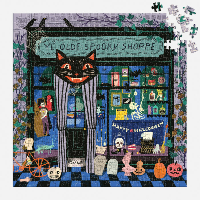 The Anne Bentley Ye Olde Spooky Shoppe 500 Piece Puzzle features a Halloween shop with skeletons, pumpkins, spooky décor, a black cat sign, and "Happy Halloween" banner. A few pieces are missing in the top right corner.